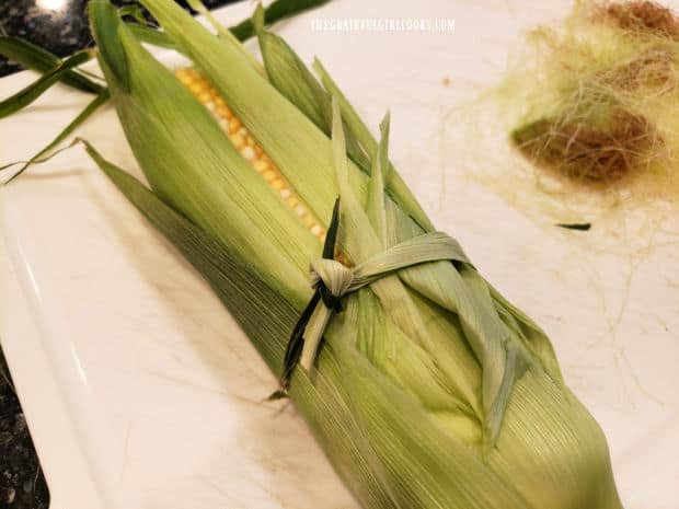 Corn husk is tied back in place using a thin piece of corn husk.