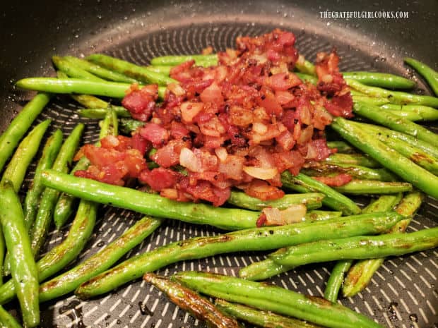 Bacon, onion and garlic mixture is added back into the skillet of green beans.