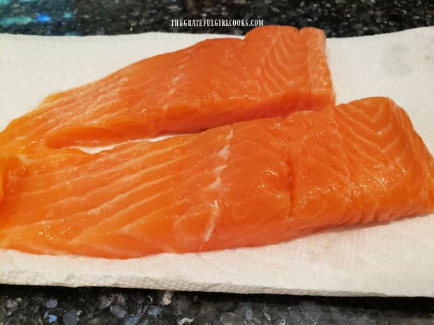 Two skinless salmon fillets laying on paper towels to absorb moisture.