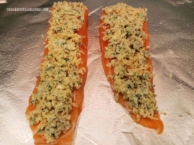 Two salmon fillets, laying on aluminum foil, covered with cheese herb topping.