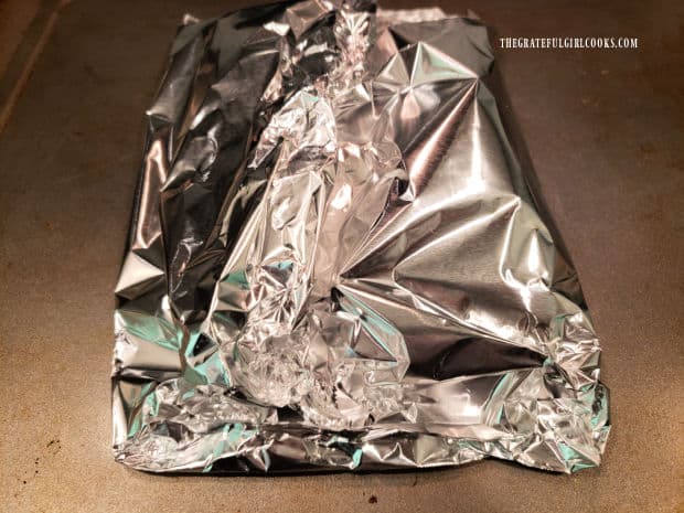 Foil pouch, with herb topped salmon fillets inside is sealed before baking.