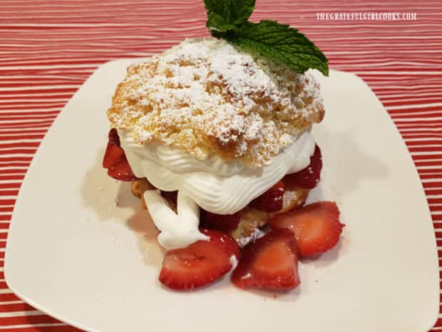 Simple strawberry shortcake, with mint garnish, served on a white plate.