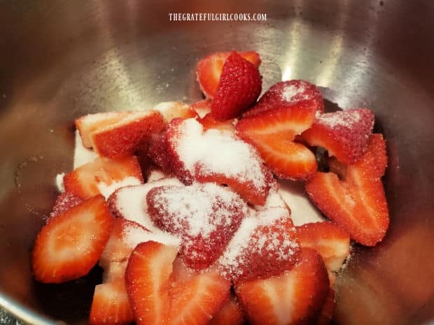 Granulated sugar and water are added to sliced fresh strawberries in bowl.