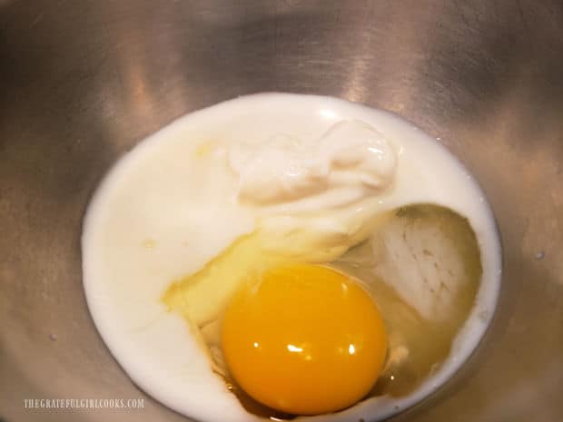 Milk, sour cream, one egg and vanilla are combined in a metal bowl.