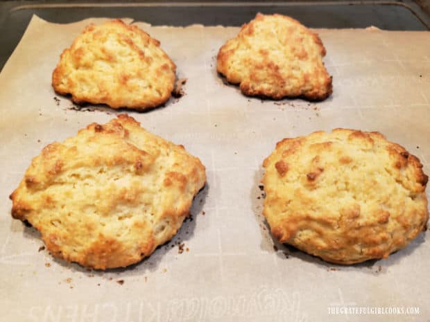 Four baked shortcakes, golden brown on top, resting on parchment paper.