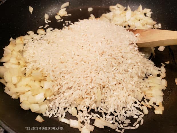 Uncooked long grain white rice is added to the onions in skillet.