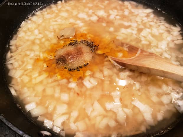 Water, hot sauce and spices are added to the onions and rice in skillet.