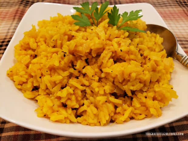 Spiced yellow rice is served, garnished with parsley, in a white bowl.