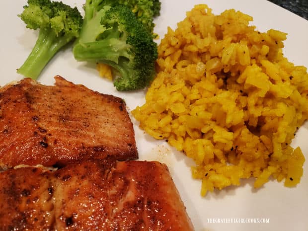 Salmon, broccoli, and spiced yellow rice, served on a white plate.