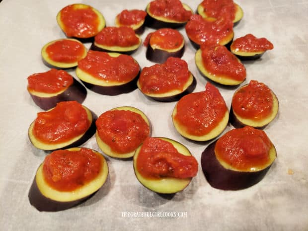 A tiny spoonful of marinara sauce is spooned on top of each eggplant slice.