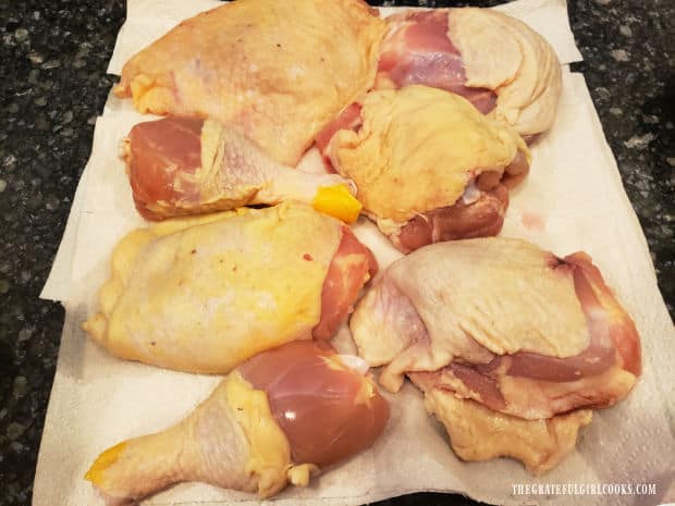 Chicken thighs and legs are patted dry using paper towels.