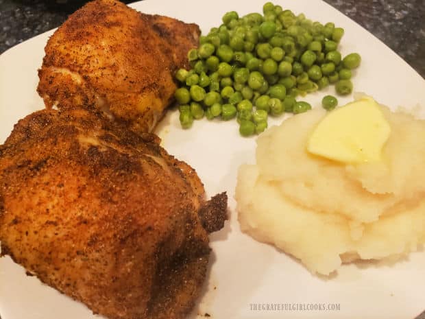 Mashed potatoes and peas are served on plate with two baked chicken thighs.