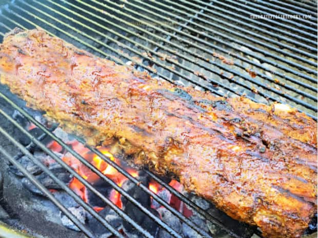 Baked grilled baby back ribs cooking over a hot BBQ grill.