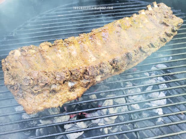 Rack of ribs is placed, BBQ sauce side down on a hot BBQ grill.