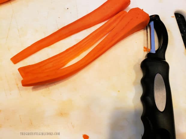 A vegetable peeler is used to slice long thin ribbons from fresh carrots.