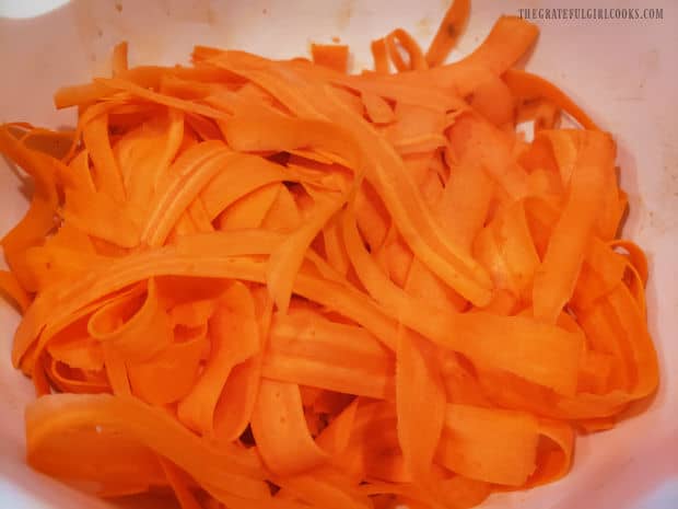 Thinly sliced carrot ribbons in a large white mixing bowl.