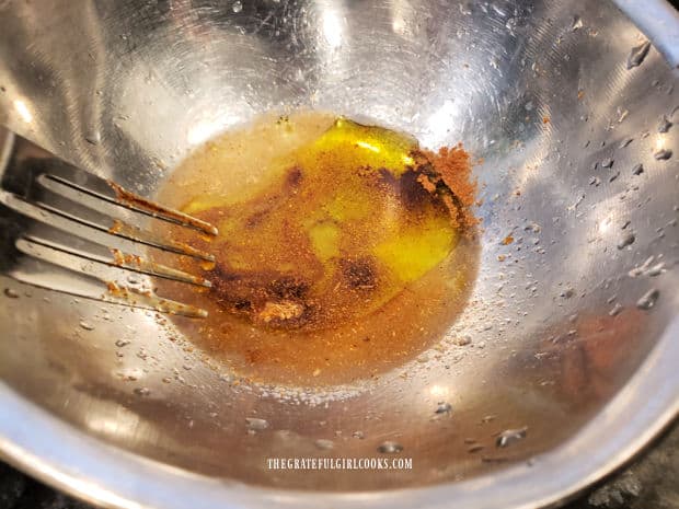 A fork is used to combine lemon juice, olive oil and spices in a metal bowl.