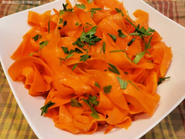 Carrot ribbon salad in a white bowl, and garnished with chopped fresh parsley.