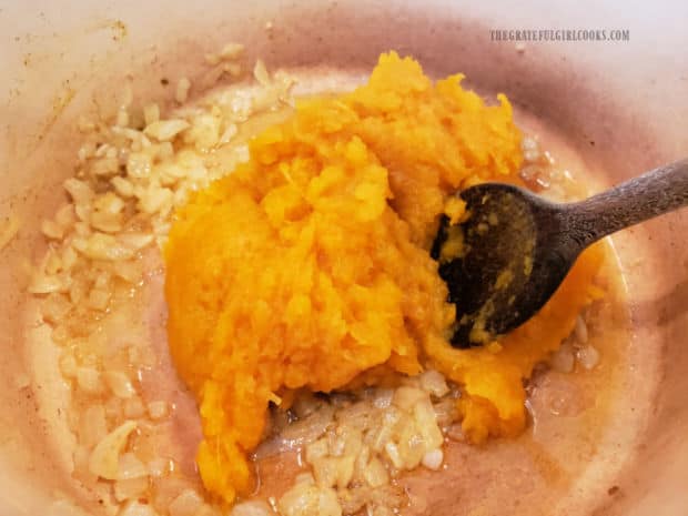 Pumpkin puree is added to the seasoned onions in the soup pot.