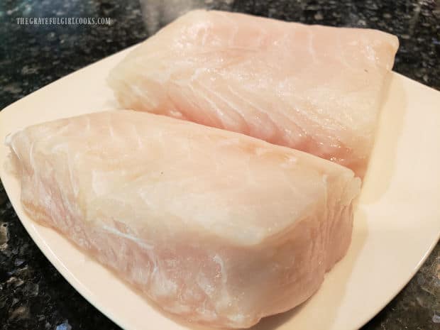 Two halibut fillets on a white plate, after being patted dry.