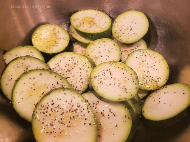 Olive oil, salt and pepper is drizzled on the sliced zucchini and tossed to coat.