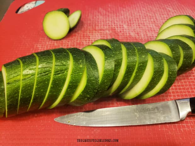 A zucchini is cut into slices before seasoning and grilling.