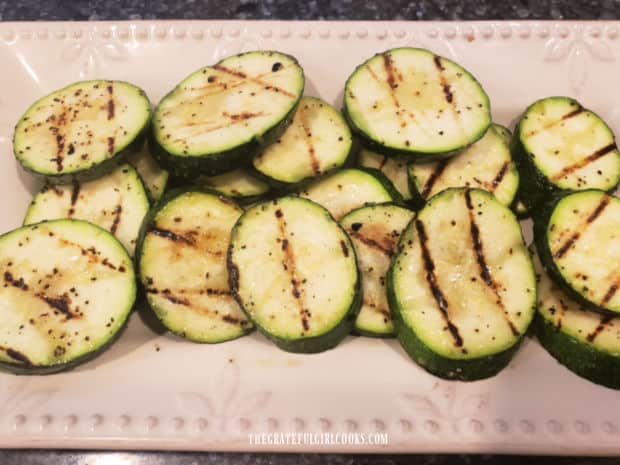 Grilled Herb Garlic Zucchini slices are transferred to a serving platter.