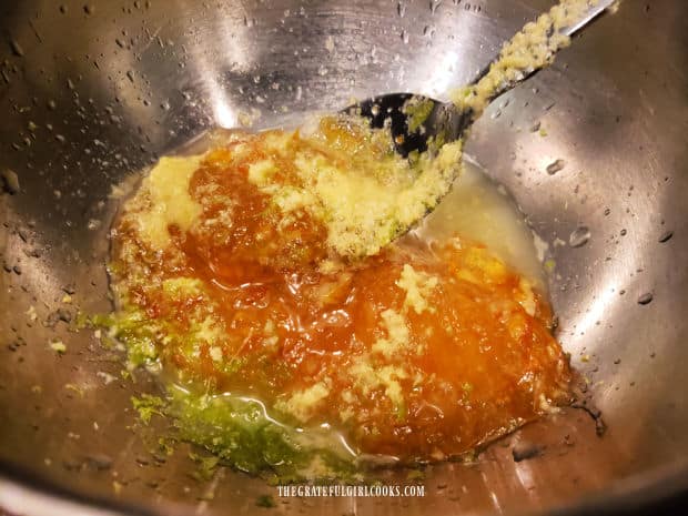 Orange marmalade, lime juice, lime zest and grated ginger are mixed in a metal bowl.