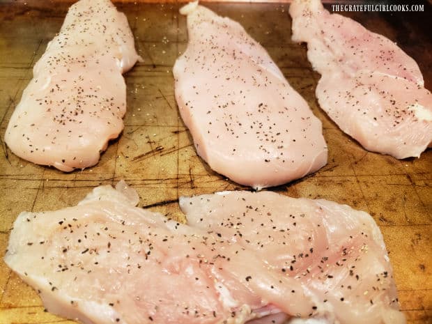 Four boneless chicken breasts are seasoned with salt and pepper.