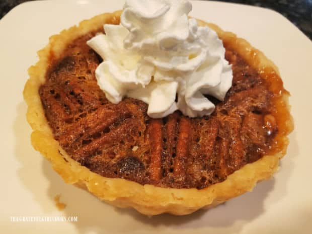Little pecan pies for two, served on a white plate, with whipped cream on top.