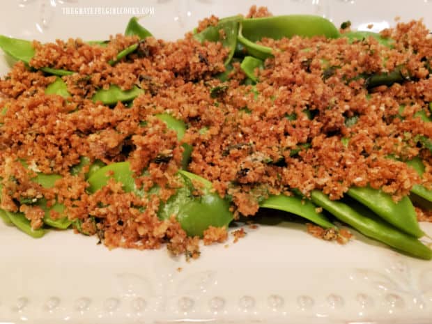 Breadcrumb topping is added to the top of cooked sugar snap peas.