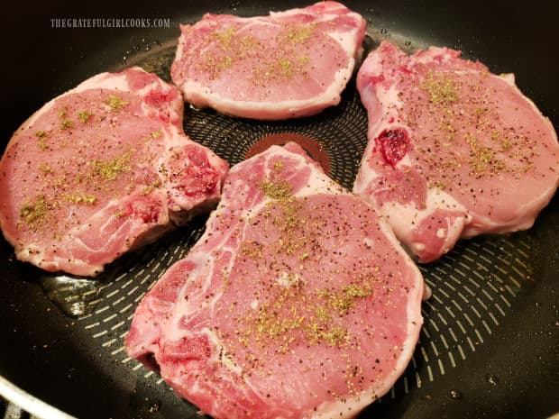 Four pork chops are pan-seared in hot oil in a large skillet.