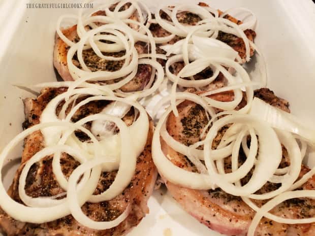 Thin onion ring slices are placed on top of the pork chops.