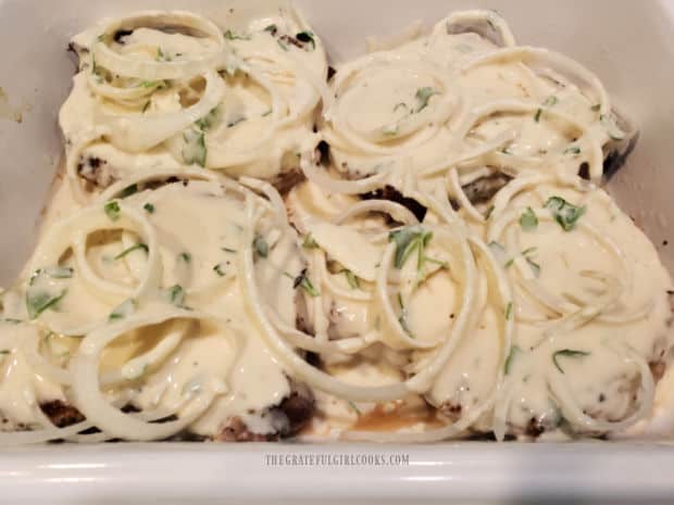 Sour cream sauce is poured over the onion topped pork chops in dish.