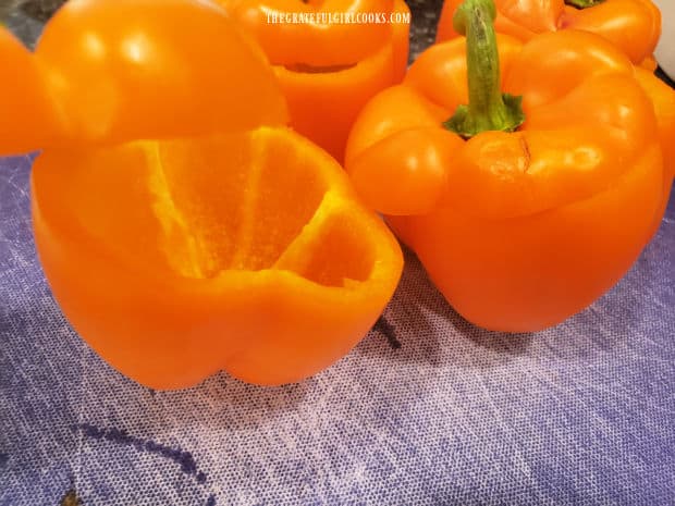 The tops of four orange bell peppers are sliced and removed.
