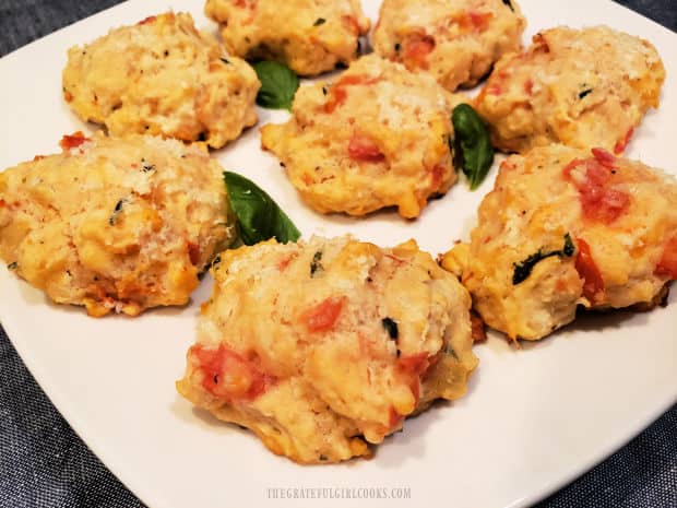 Eight Tomato Basil Drop Biscuits, with basil leaves, served on a white plate.