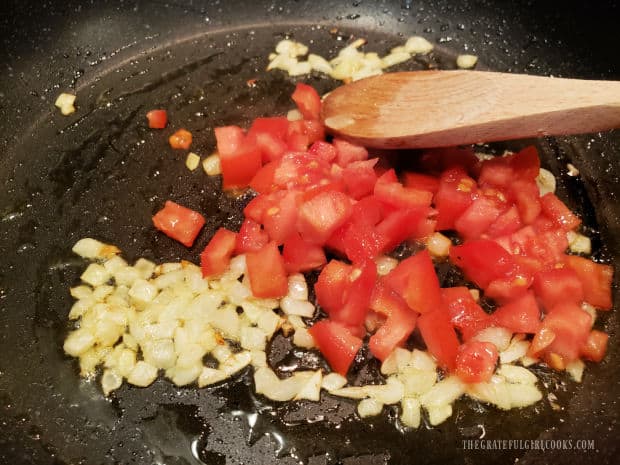 Fresh, chopped tomatoes are added to the cooked onion in the skillet.