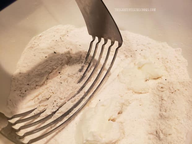 Vegetable shortening is cut into the dry ingredients in a large bowl.