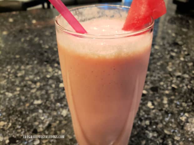 A glass of watermelon pineapple smoothie with a straw and watermelon wedge.