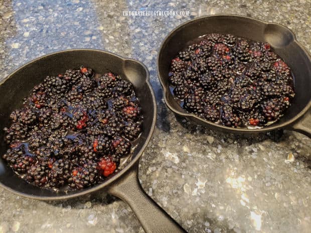 Two, 6" cast iron skillet with blackberry cobbler filling in them.