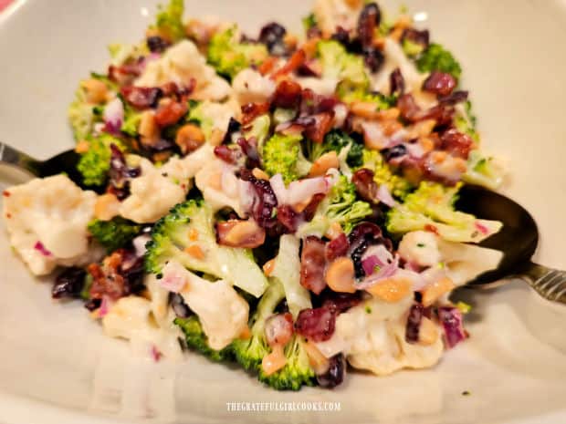 A white bowl, filled with cauliflower broccoli bacon salad.