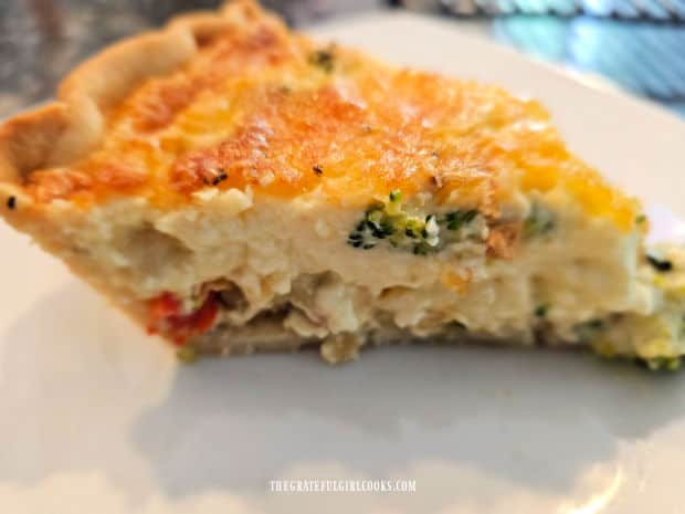 One slice of vegetable cheddar quiche, served on a white plate.