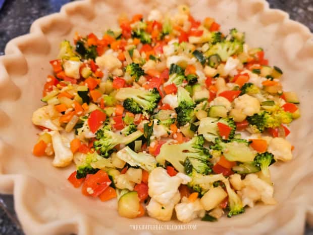 Cooked veggies are added to an unbaked pie crust.