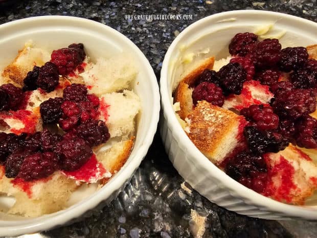 A layer of bread cubes and blackberries in a buttered ramekin.