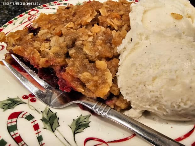 A serving of blackberry pecan crisp on a plate, with a scoop of vanilla ice cream.