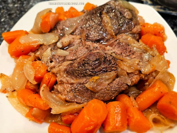 Classic pot roast on white platter, with onions and carrots on the side.