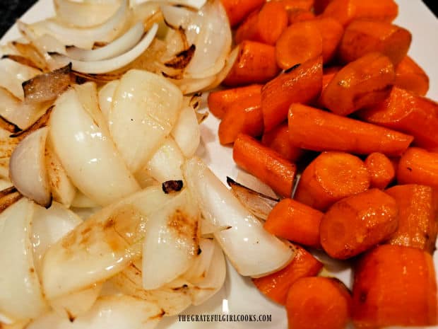 Lightly browned onions and carrots rest on a plate after being cooked.