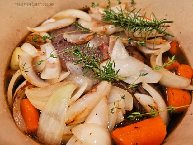 Pot roast, onions, carrots and fresh herbs are ready to be baked.
