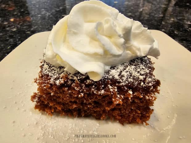 Slice of homemade gingerbread, served with whipped cream, on a white plate.