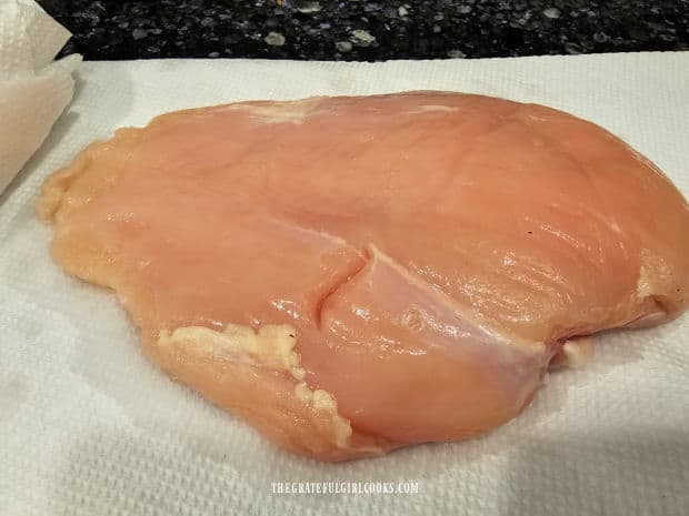 A chicken breast is blotted dry with paper towels before basting.